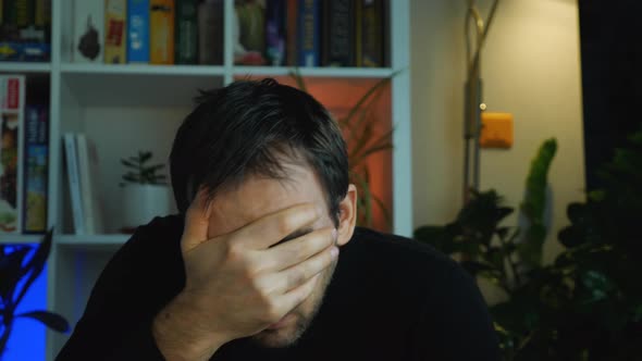 Close-up of a blue-eyed man watching horror on TV. Fear covers his mouth and eyes with his hand