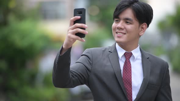 Young Handsome Asian Businessman Using Phone in the Streets Outdoors