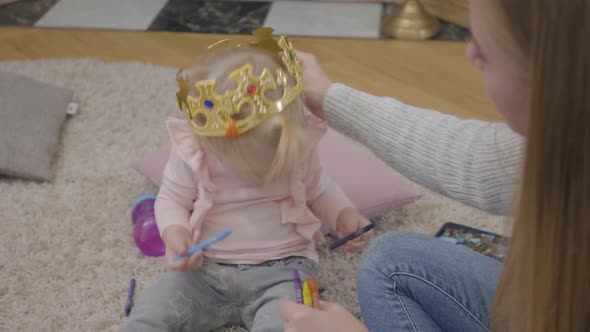 Close-up of Young Caucasian Mother Trying To Put Toy Crown on Daughter's Head