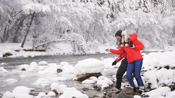 A Young Happy Family Stands at the Mouth of a Mountain River. Couple in Love Throws Pebbles