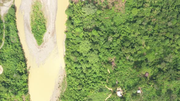 Following a large river in a tropical rainforest with many metal colored tin roofs 