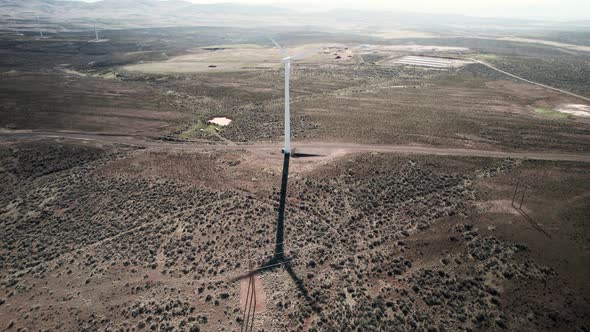 High angle wide aerial orbit of a wind generating electric turbine spins in a desert