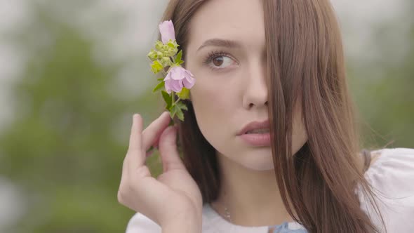 Portrait of Attractive Young Brunette Girl Holding Pink Flower Near Her Ear Looking Away