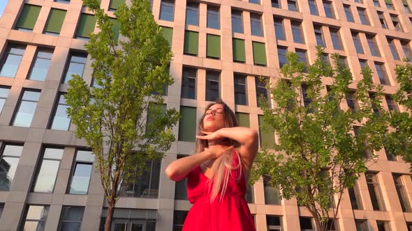 Beautiful Young Girl Dancing on the Street of a Modern Building of a Business Center in the Sunset