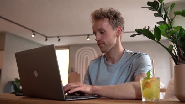 Attractive guy sitting at the table and working on a laptop. The young man respects his work