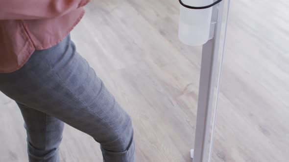 Businesswoman using foot pump sanitizer to disinfect hands as she enters the workplace