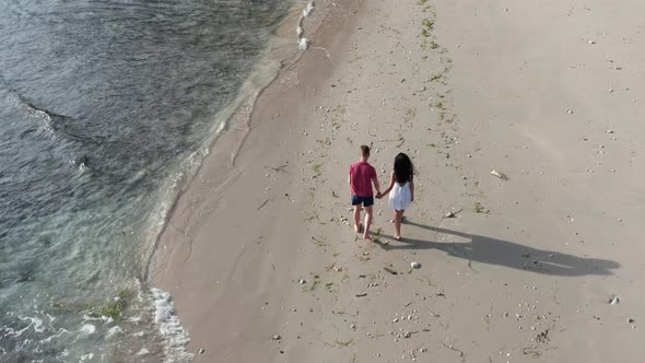 Man and Woman Walking Along Tropical Beach at Sunset, Tracking Aerial Shot