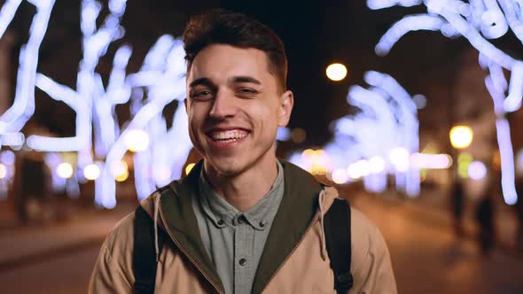 Portrait of Happy European Man 20s Laughing While Walking Through Evening City Street with Bright