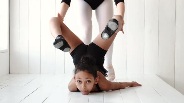 Female Ballet Teacher Helping Girl Warm Up Before Performance