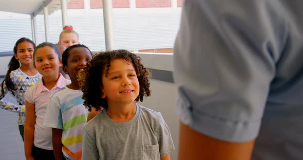 Schoolkids with teacher standing in row in hallway at school 4k