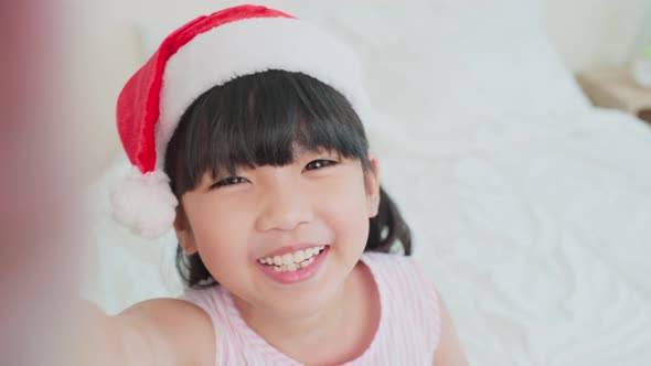 Portrait of Asian young girl wear Santa hat, using mobile phone video call in bedroom at home.