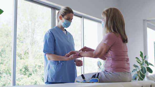 Female health worker stretching wrist of senior woman at home