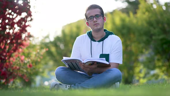 University student sitting on grass, writing essay, literary studies project