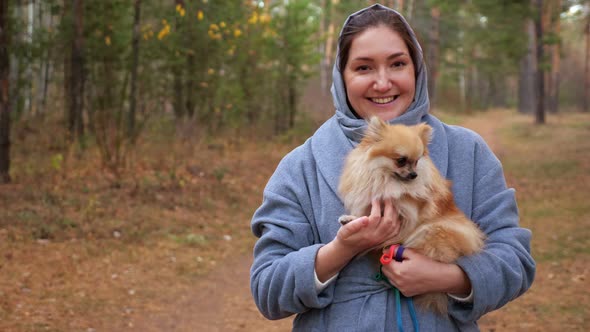 Young Woman Holding Pomeranian Mini Spitz in Arms While Walking in Autumn Park Slow Motion