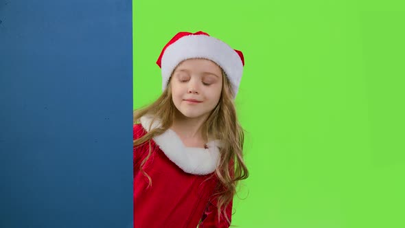 Child Girl Peeking Out From Behind the Blue Board. Green Screen