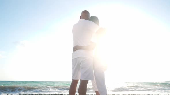 Wide Shot of Hugging Asian Man and Senior Woman Standing in Sunshine on Beach with Turquoise Foamy