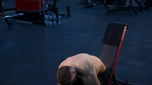 Bodybuilder with perfect body and strong hands trains with dumbbells. Dark background of modern gym.