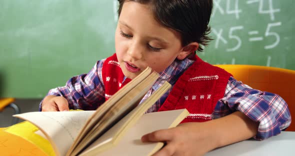 Schoolboy reading book in classroom at school