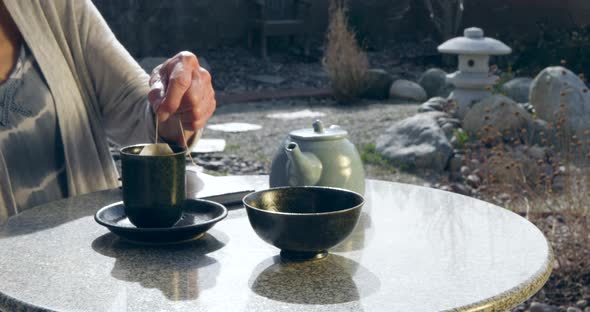 A woman reading a book then ring an herbal tea bag from hot water in a teacup and drinking.