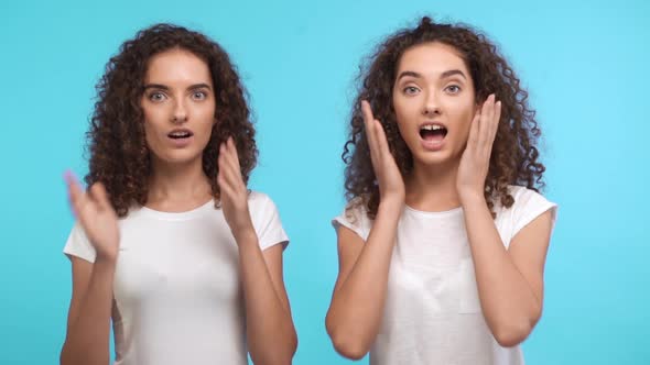 Two Young Beautiful Curly Female Caucasian Twins in White Tshirts Looking at Camera in Amazement on