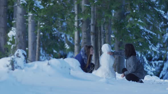 Girls building a snowman in the forest