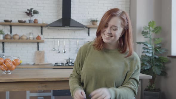 Portrait of Positive Plussize Woman Sitting in Kitchen Smiling at Camera