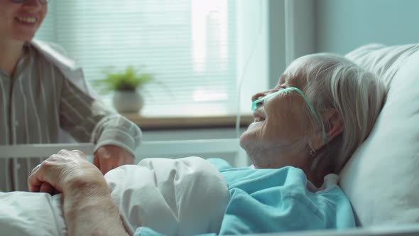 Daughter Cheering Senior Mother in Hospital Ward