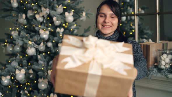 Portrait of Beautiful Brunette Giving Present on Christmas Day Standing Indoors at Home with