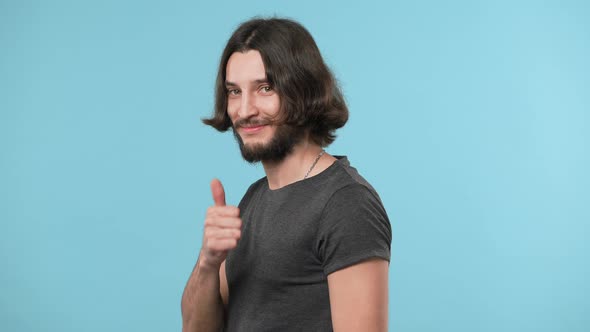 Halfturn Portrait of Positive Bearded Guy in Casual Gesturing Good Sign Thumb Up with Pleasure Over