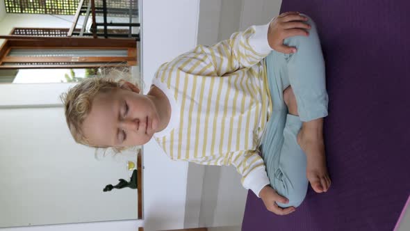 Vertical Video with a Child Who Sits in a Halflotus Position on a Rug with His Eyes Closed in