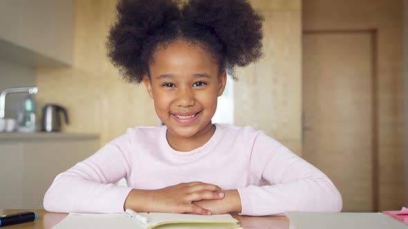 Smiling Afro American Schoolgirl Engaged in Distance Learning Looking at Camera