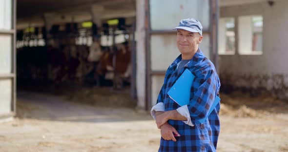 Farmer Gesturing While Writing on Clipboard Against Barn