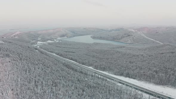 Drone Flight Over a Winter Forest and a Highway Among the Hills in the Evening