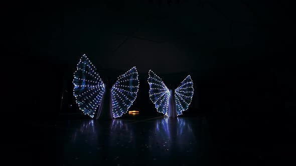 The Girls Perform a Dance with LED Wings. LED Lights Glow in the Dark. Young Girls Revolve Around