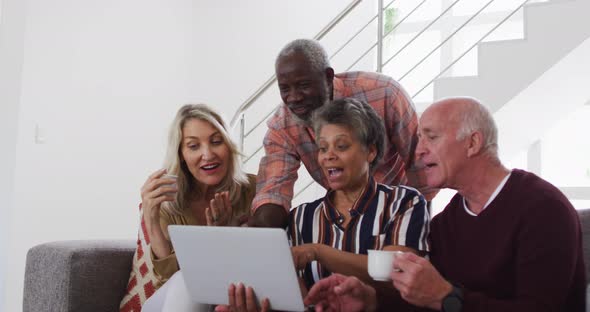 Two diverse senior couples sitting on a couch using a laptop and laughing