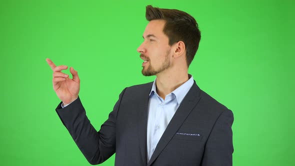 A Young Handsome Businessman Talks To the Camera and Points at Objects Falling Around Him