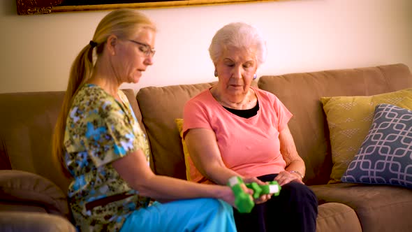 Home healthcare therapist helping elderly woman with physical therapy with hand weights.