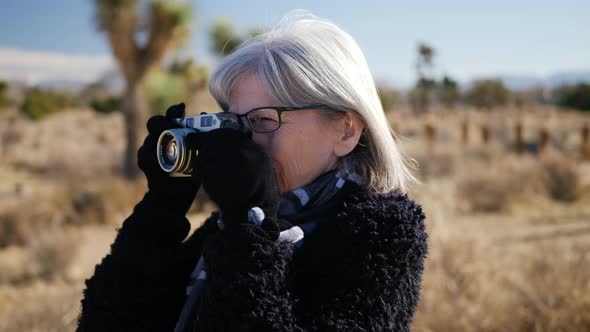 An adult woman photographer taking pictures with her old fashioned film camera and lens in a desert