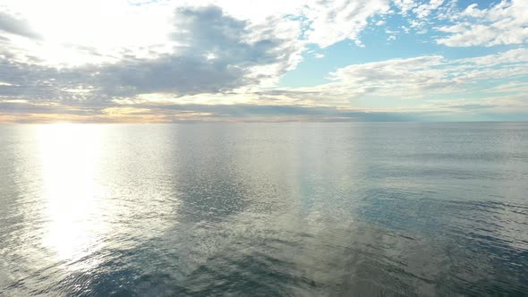 AERIAL: Flying Backwards with Calm and Peaceful Sea with Reflection of Sky and Cloudy Sky