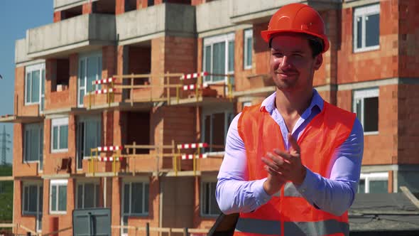 Happy Construction Worker Applauds with Hands in Front of Building Site