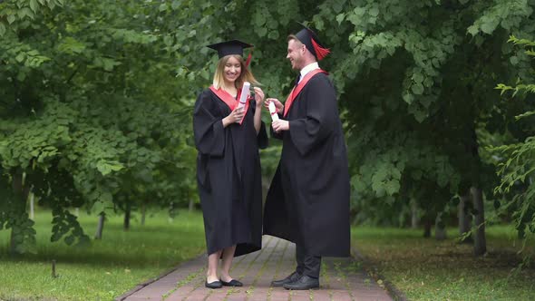 Happy Graduates Holding Diplomas and Talking in Park After Graduation Ceremony