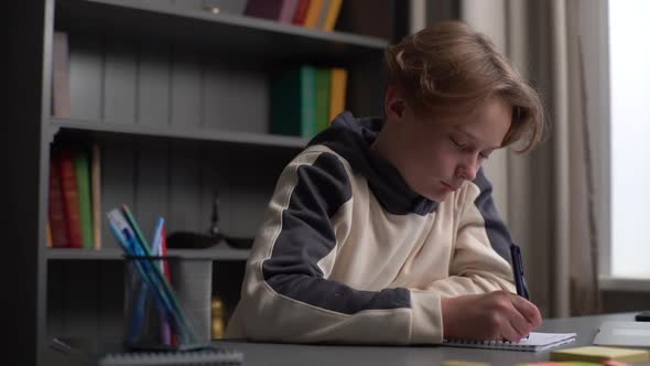 Closeup Portrait of Exhausted Pupil Boy Doing Homework Taking Notes in Workbook and Falling Asleep