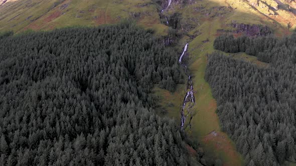 Aerial view of a green wood in the highlands in Scotland and a waterfall on t