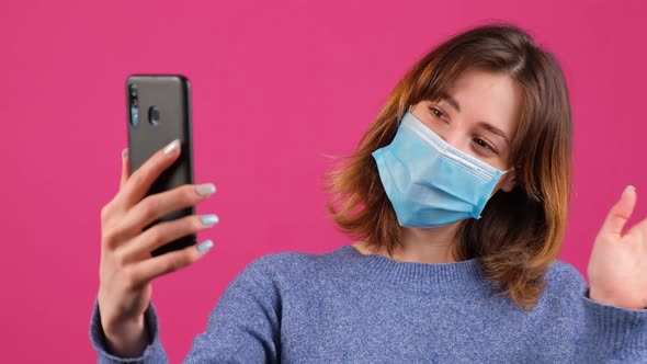 Young Woman Greets Friends During Online Conversation Wearing Medical Mask