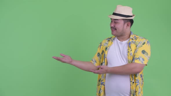 Happy Young Overweight Asian Tourist Man Showing Something and Giving Thumbs Up