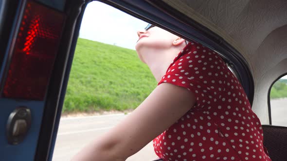 Happy Girl in Sunglasses Leaning Out of Vintage Car Window and Enjoying Trip