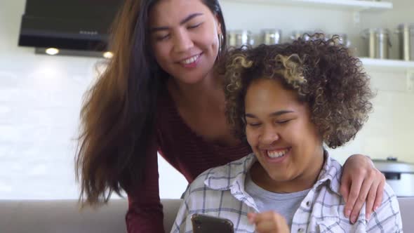 A Girl Hugs Her Friend From Behind Who is Holding a Smartphone