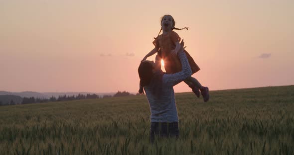 mother and young daughter walking and playing in a field during sunset