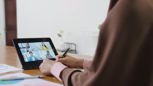 Asian muslim lady using tablet talk to colleagues in video call while work from home.