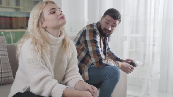 Angry Bearded Caucasian Guy Shouting at Blond Woman From the Background. Husband Blaming Cheating